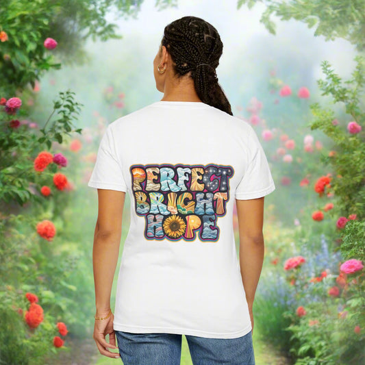 A person wearing a white unisex garment-dyed T-shirt with a sunflower graphic on the front and a  perfect bright hope message on the back.