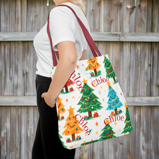 Person holding a tote bag with Christmas tree design and personalized text.